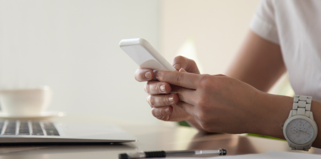 hombre con celular en sus manos, frente al computador